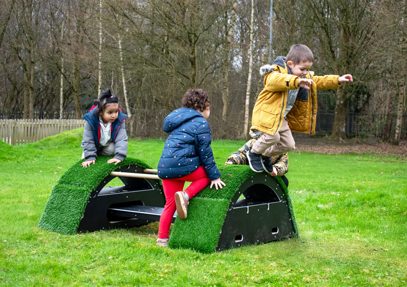 Three children playing and jumping on grass-topped blocks, The Rockies